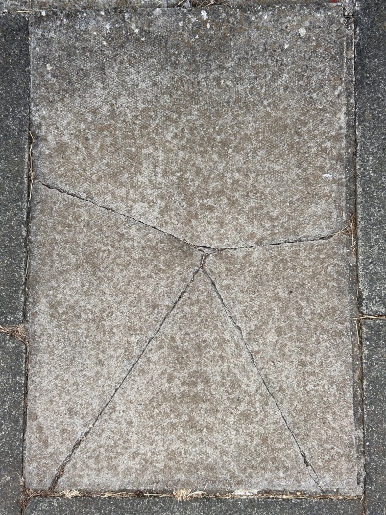 A top down photo of a cracked paving slab, resembling a stylised figure of a person with upreaching arms.